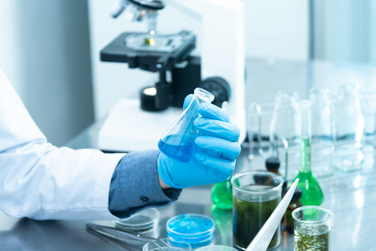 Lab technician holding a blue liquid sample in front of a microscope during a drug analysis procedure