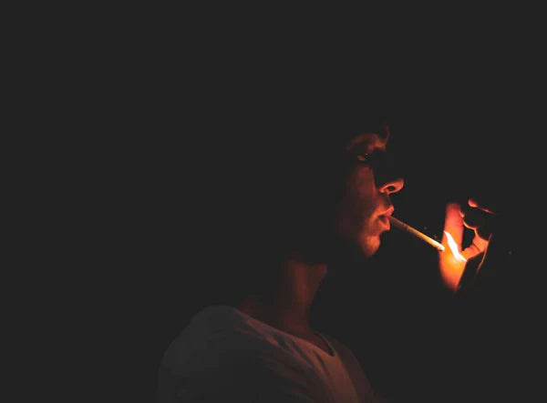 A man lighting a cigarette in a dark room