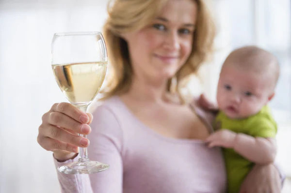 A woman holding a baby in one hand an an alcoholic drink in the other 