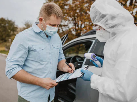 A driver wearing a mask and a man in a hazmat suit standing next to a car discussing DOT drug tests