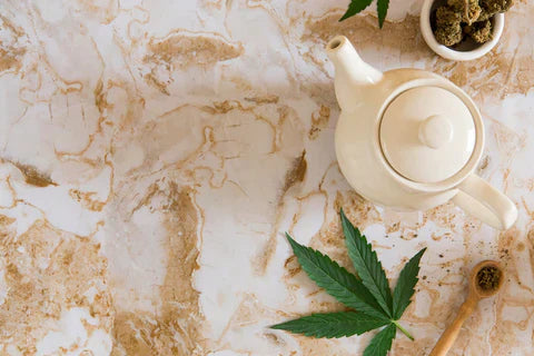 A cannabis leaf next to a detox tea pot laid on a marble table surface 