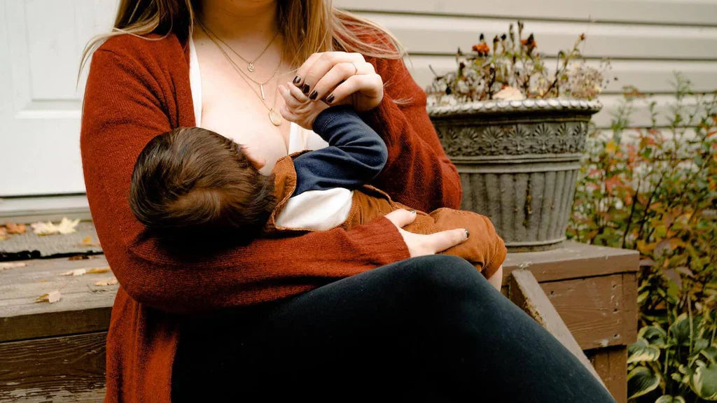 A woman sitting on a bench, breastfeeding a child 