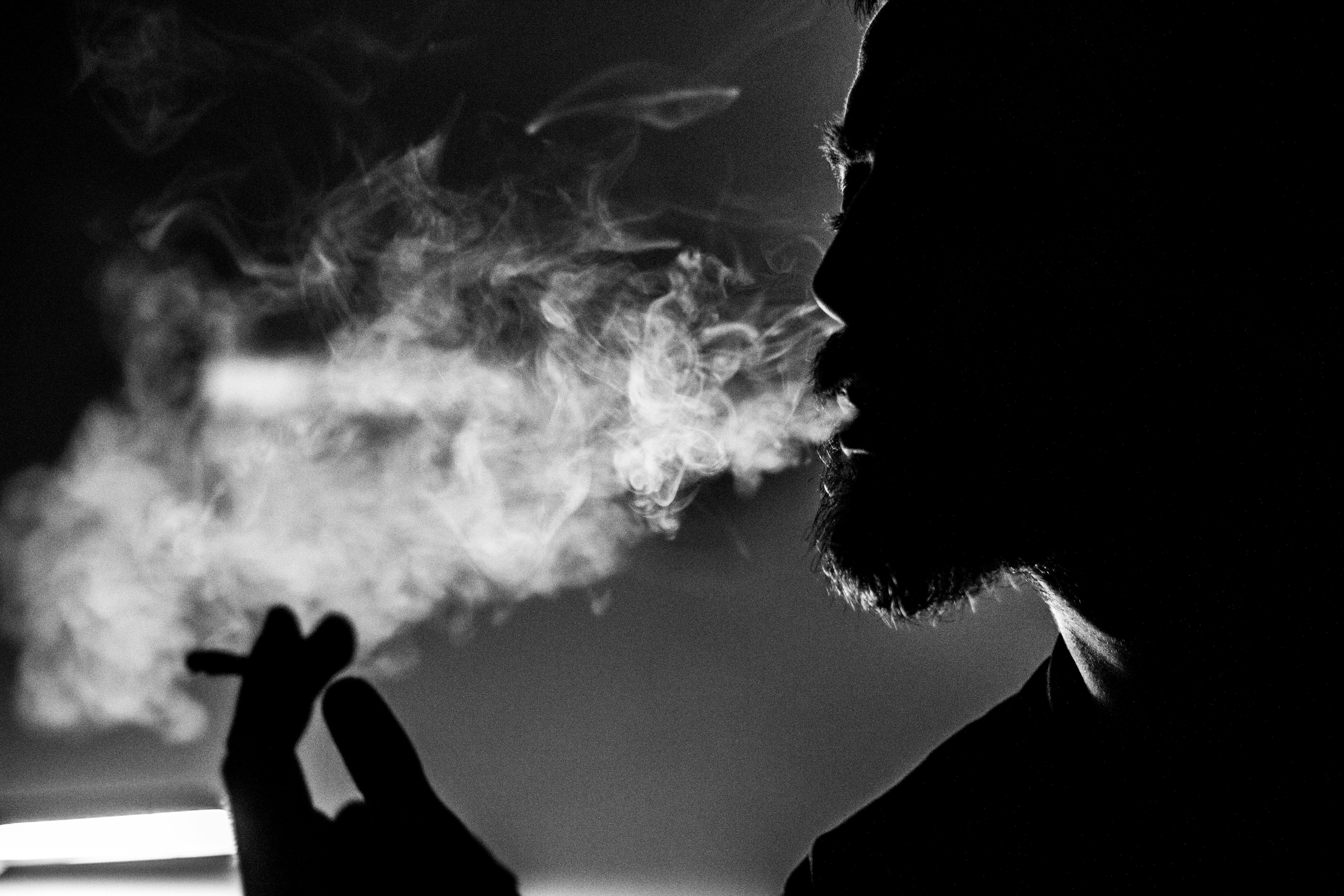 An obscured closeup of a man smoking, causing sedondhand smoke to go all around him 
