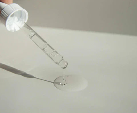 A closeup of a dropper dropping transparent liquid on a white surface